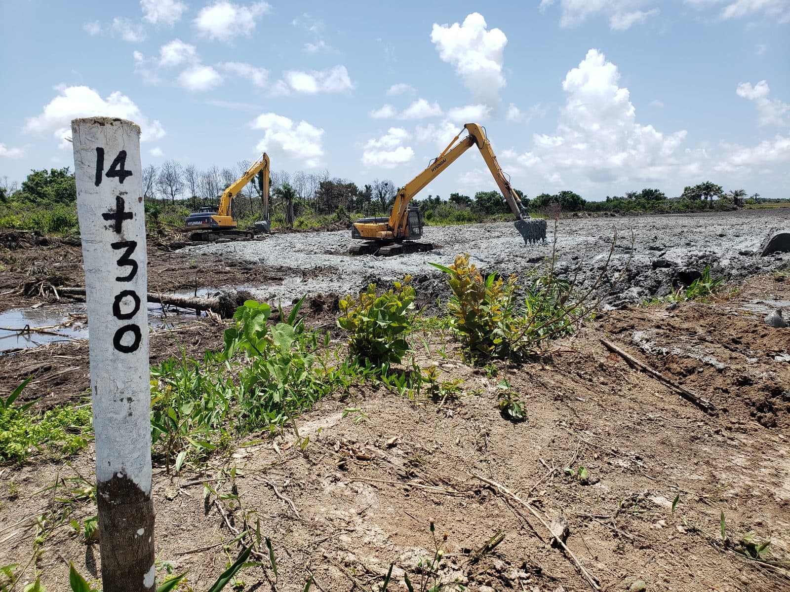 Survey chainage marker reading 14+300 in the foreground with long-reach excavators dredging behind